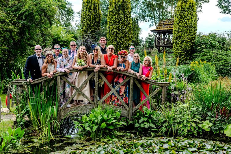 Guests at garden wedding venue gather on bridge over pond filled with lilly pads