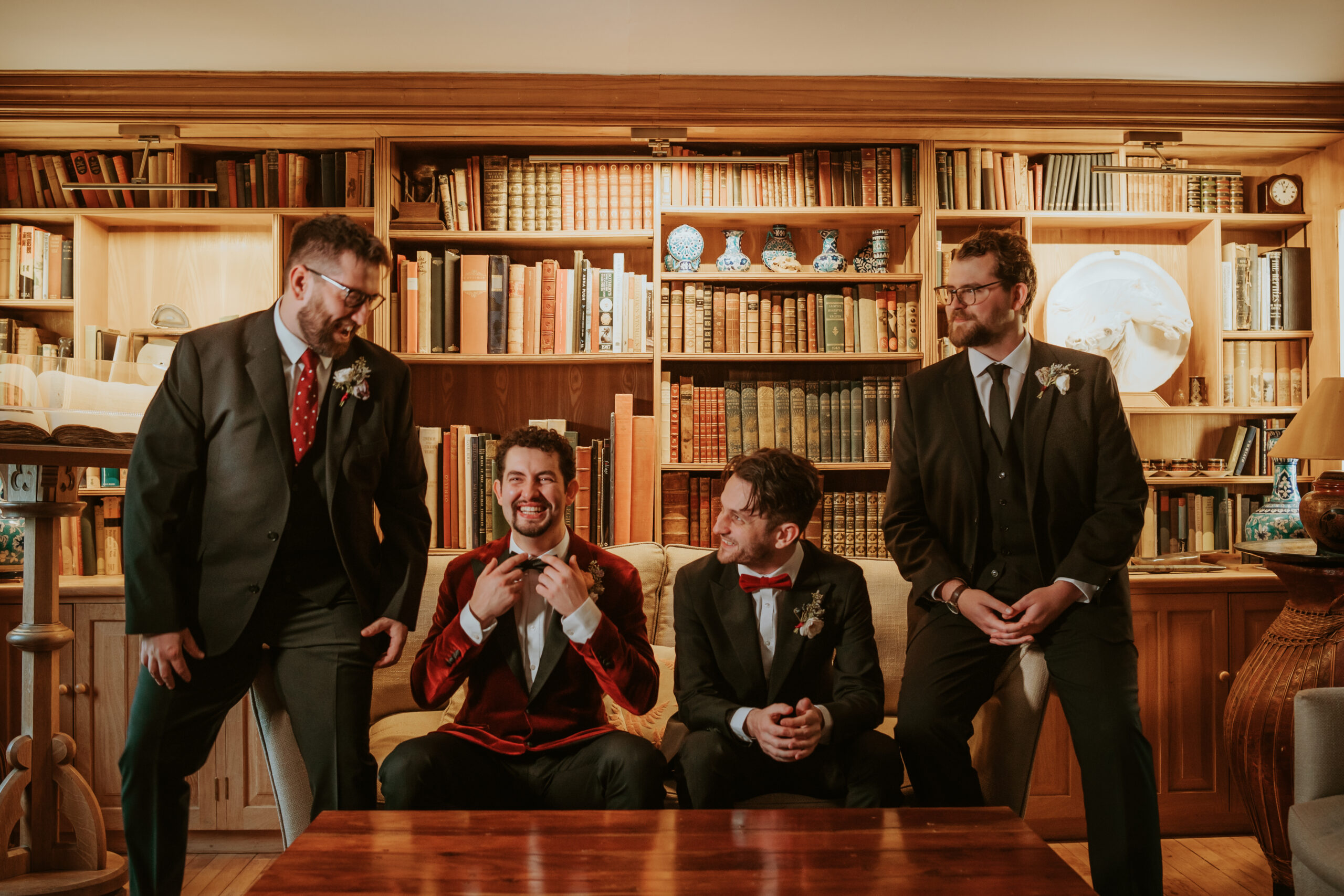 Groom & Groomsmen at country house wedding venue seated on sofa in drawing room in front of book shelves