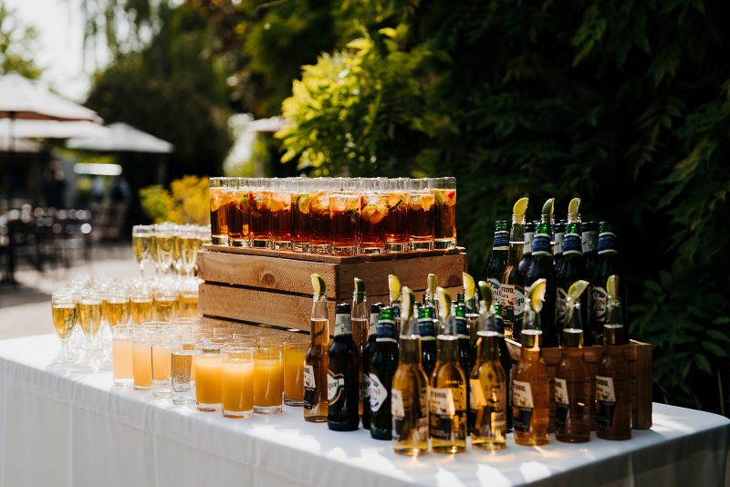 Stunning display of reception drinks on table at wedding venue including bottled beers, orange juice and fruit-filled pimms