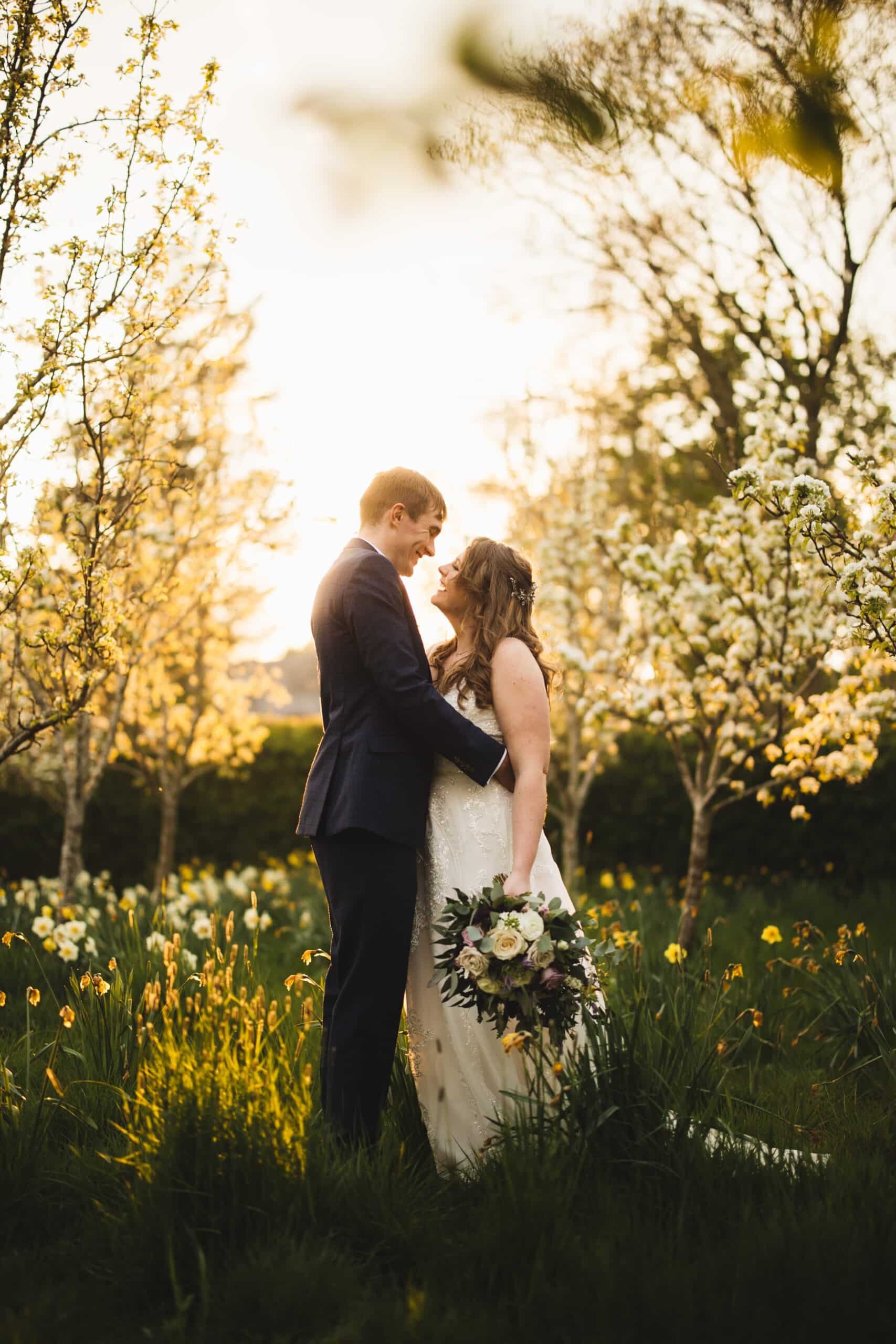 Bride and Groom standing amongst the blossoms and daffodils in the Arboretum at South Farm Cambridge wedding venue