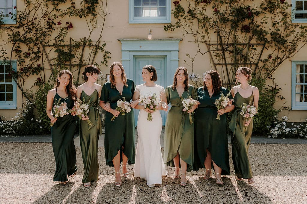 Bride and her bridesmaids in olive green dresses at the front of the charming cream farmhouse countryside wedding venue