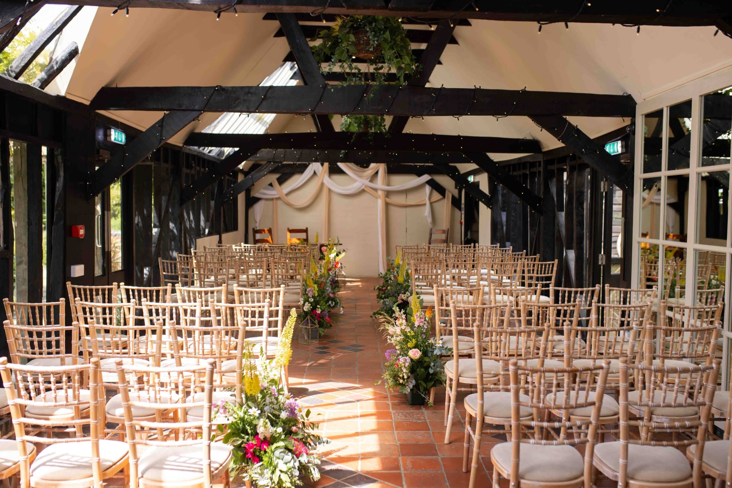 The Old Dairy set with white chivari chairs white soft draping and Spring florals at indoor ceremony barn at barn wedding venue