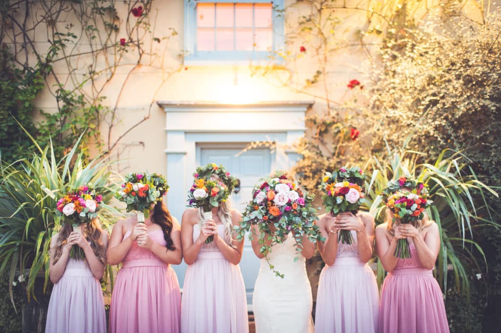 Bridesmaids and bride standing at the front of the charming Farmhouse with their bright Spring bouquets in front of their faces