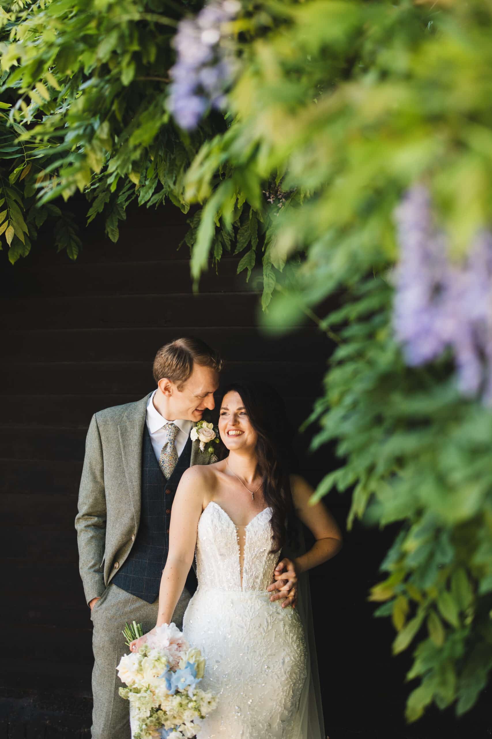 Bride and Groom standing infront of the Wisteria growing on the Sunset Terrace at outdoor wedding venue in Hertfordshire
