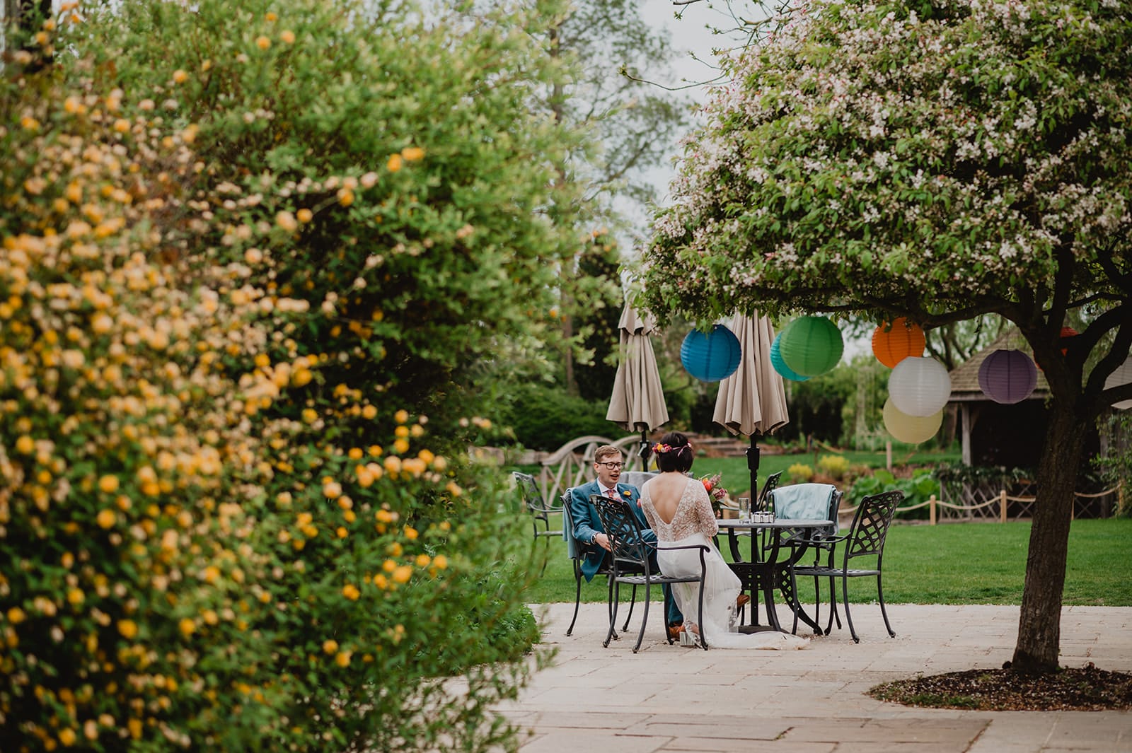 Asian Bride and Groom sitting taking it all in on the garden terrace with spring blossoms surrounding them at barn wedding venue