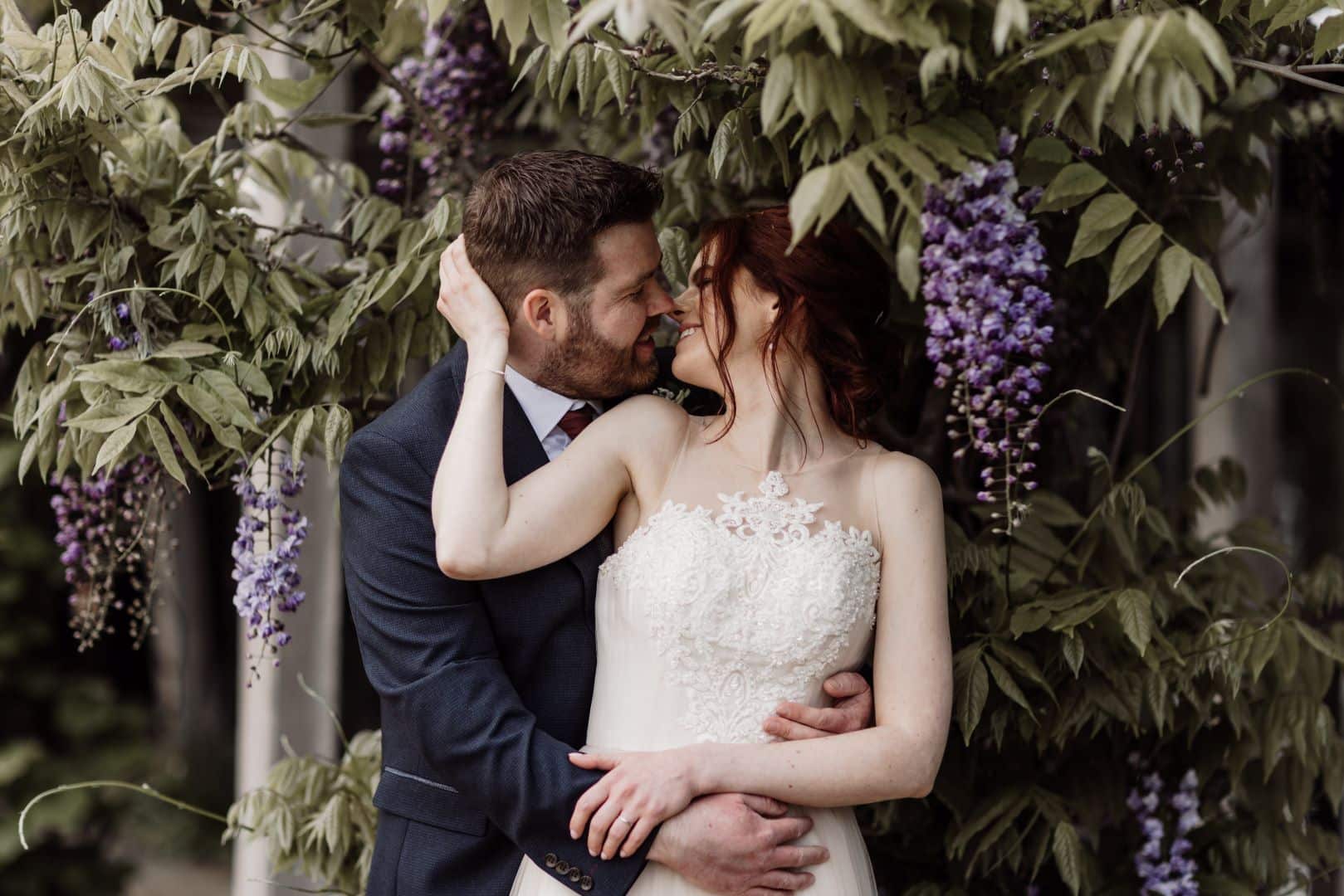 Bride and Groom kissing underneath the purple Wisteria on the Sunset Terrace at their countryside wedding venue