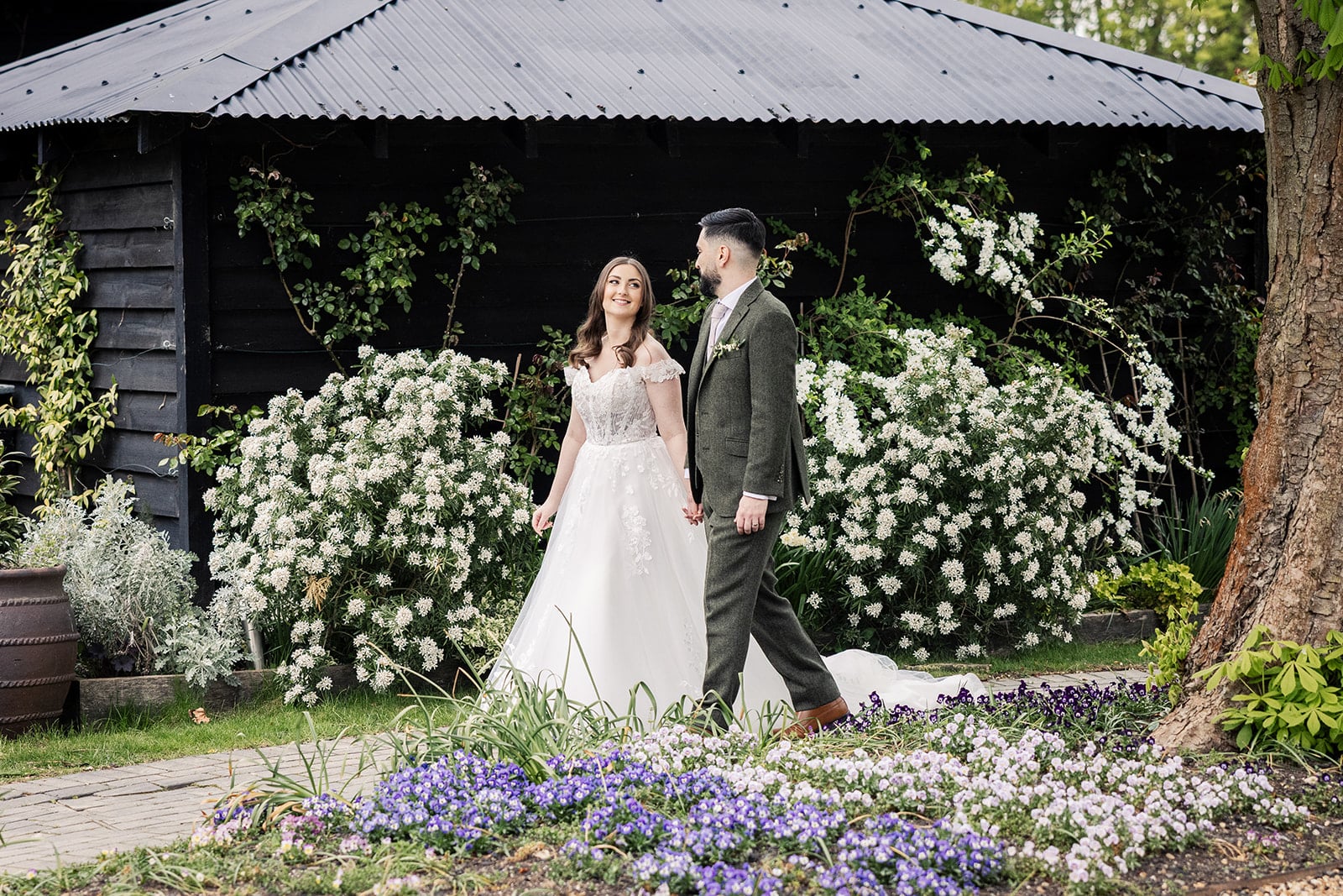 Bride and Groom walking in front of the South Farm entrance adorned with Spring blossoms at eco friendly barn wedding venue