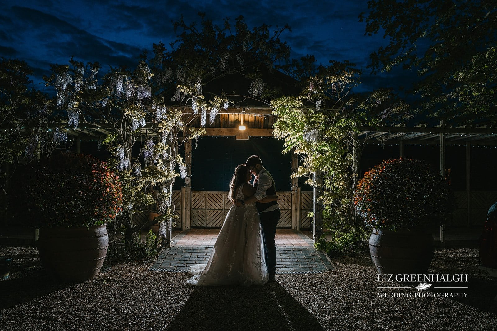 Bride and Groom standing on the Wisteria lined walkway at twilight leading through to the rustic Tudor Barn wedding venue