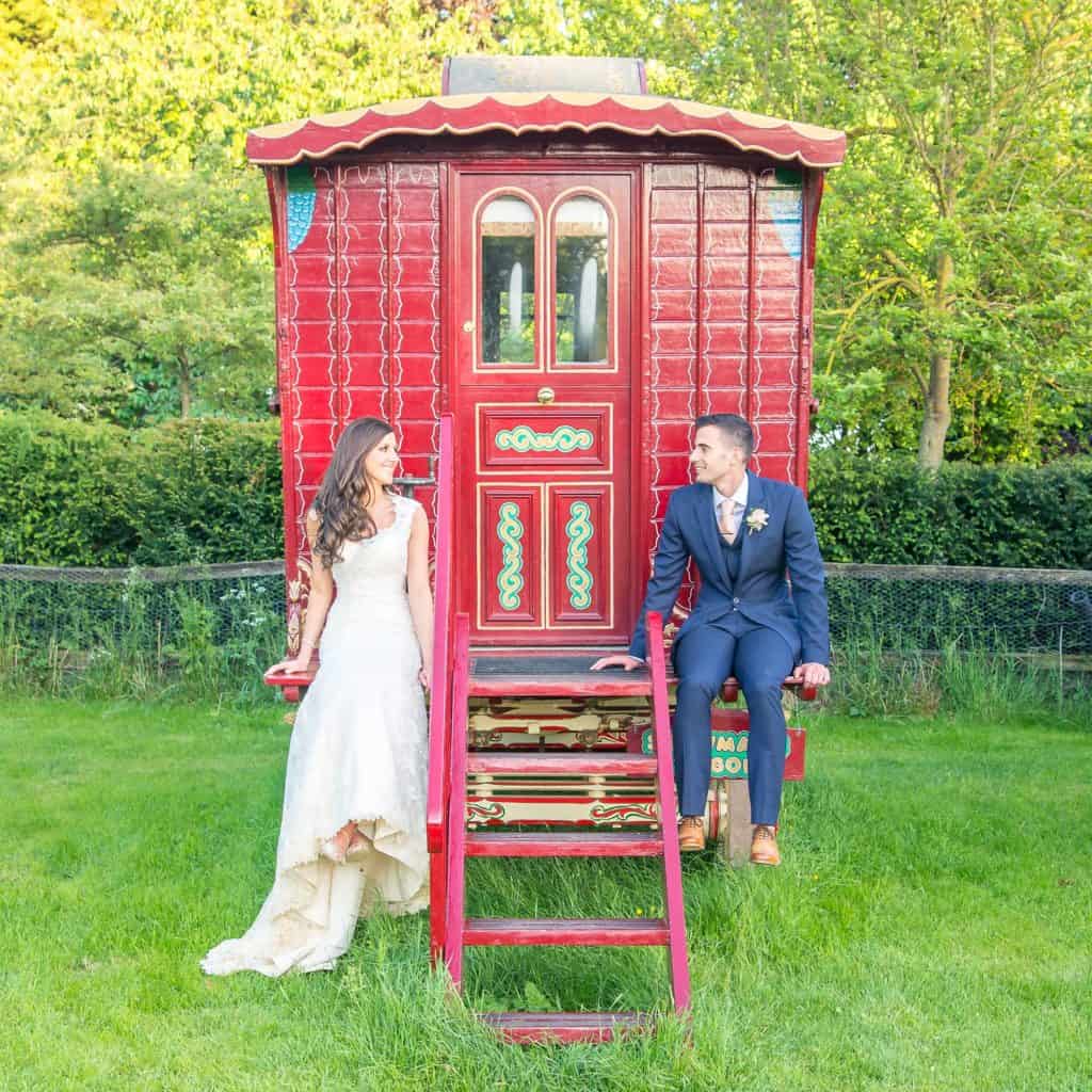 Couple sitting on steps of red romany wagon at South Farm Wedding Venue