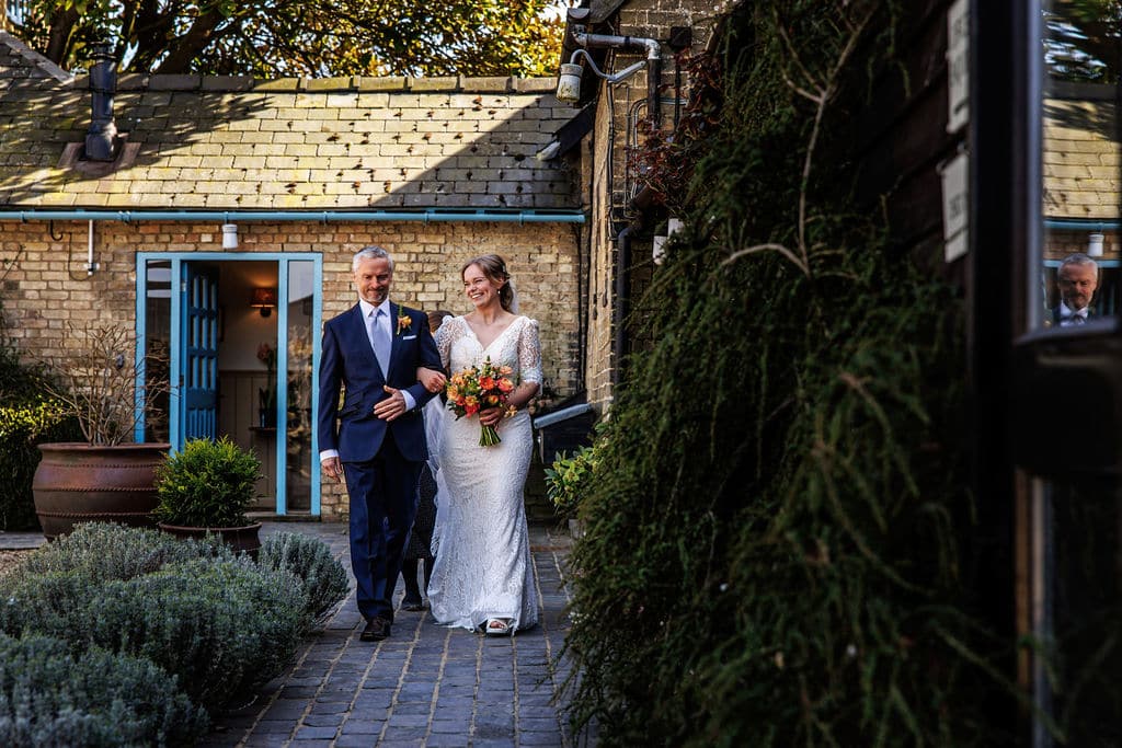 Bride and her father walking to the charming Old Dairy for their indoor Spring ceremony at barn style wedding venue