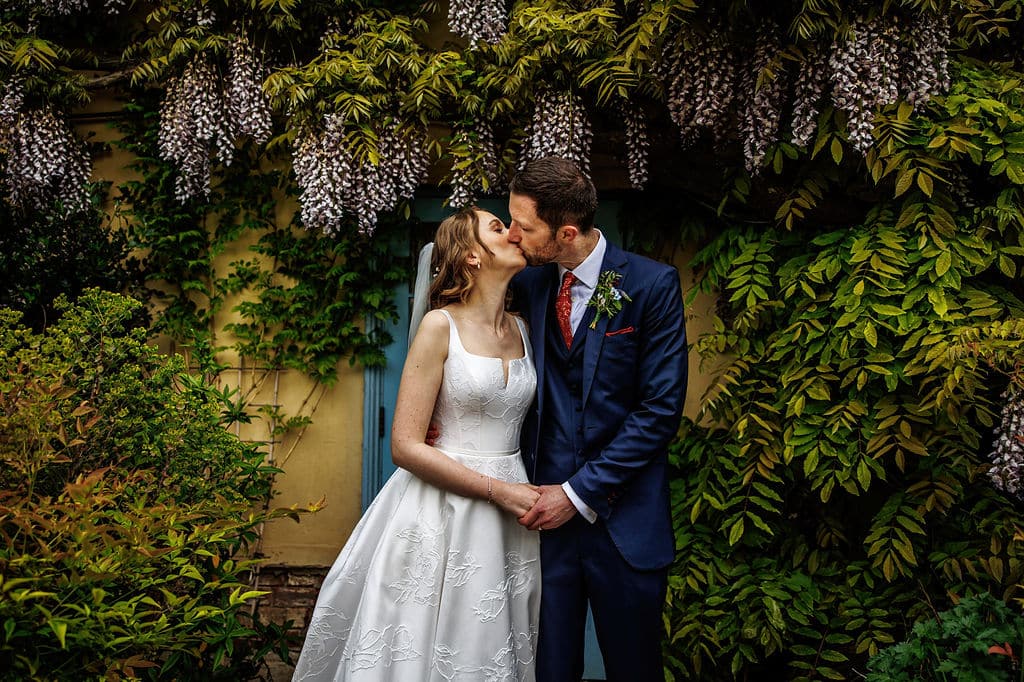 Bride and Groom sharing a kiss infront of thWisteria on the Garden Terrace at outdoor garden wedding venue