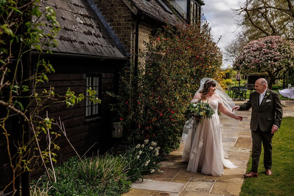 Bride and her dad walking from the Coach House Suite along the Sunset Terrace to wedding ceremony in the rustic Tudor Barn at Barn wedding venue in Hertfordshire