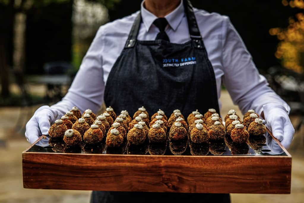 Canapes being served at outdoor wedding venue delicious arancini on a board held by a member of waiting staff in South Farm apron