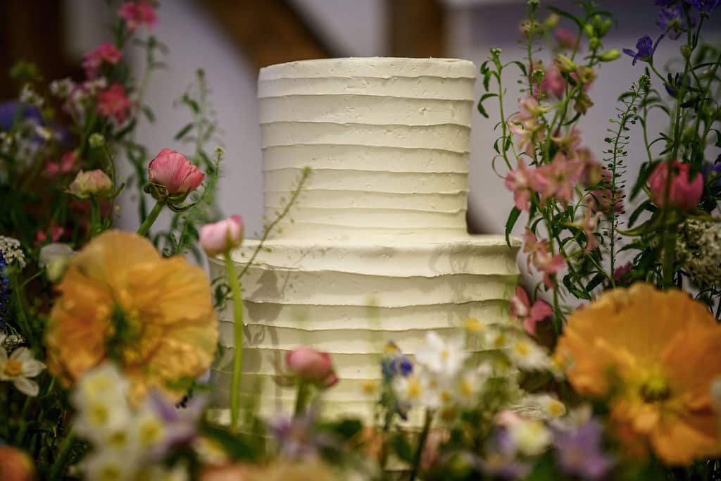 White buttercream iced two tier wedding cake surrounded by spring flowers