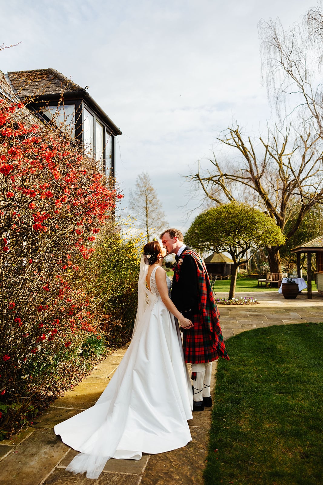 Bride and Groom in scottish kilt on the Garden Terrace with Spring blossoms behind them at country wedding venue