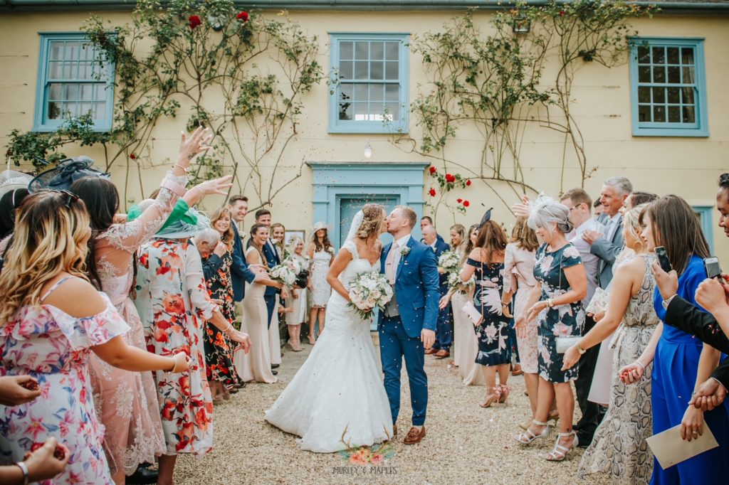 Bride and Groom kiss during confetti shower in front of beautiful country house wedding venue