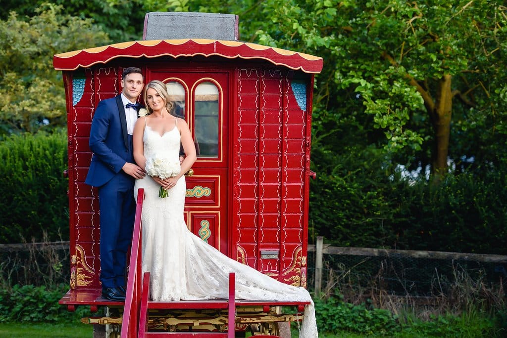 Bride and Groom on steps of red romany wagon on their wedding day