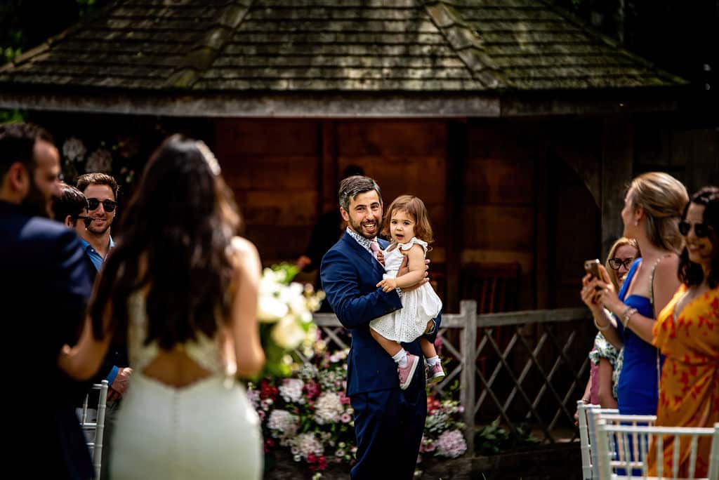 Bride enters wedding aisle to see groom and young daughter ahead 