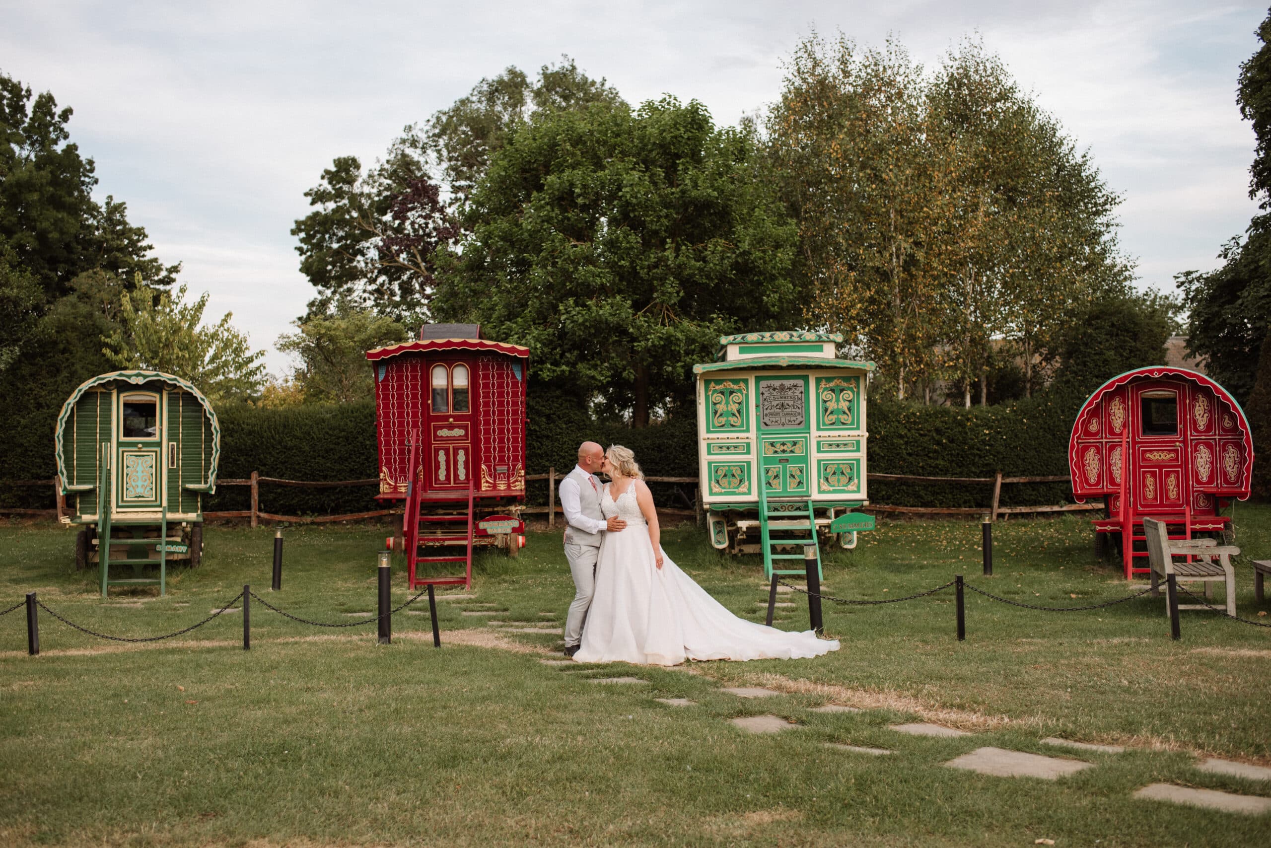 Bride and Groom in front of colourful red and green romany wagons at boho wedding venue