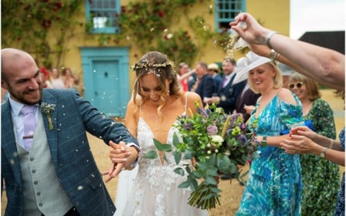 Just married bride and groom are showered with confetti at country house wedding venue