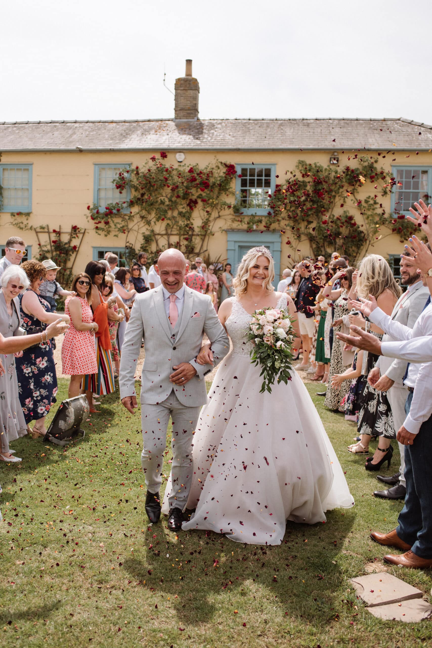 Bride and Groom have a confetti photo in front of pretty country farm house with guests
