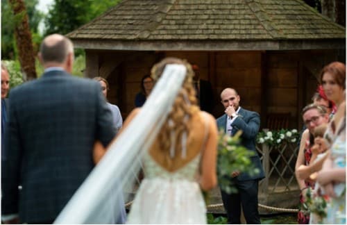 Groom waits for bride at end of aisle at garden wedding venue