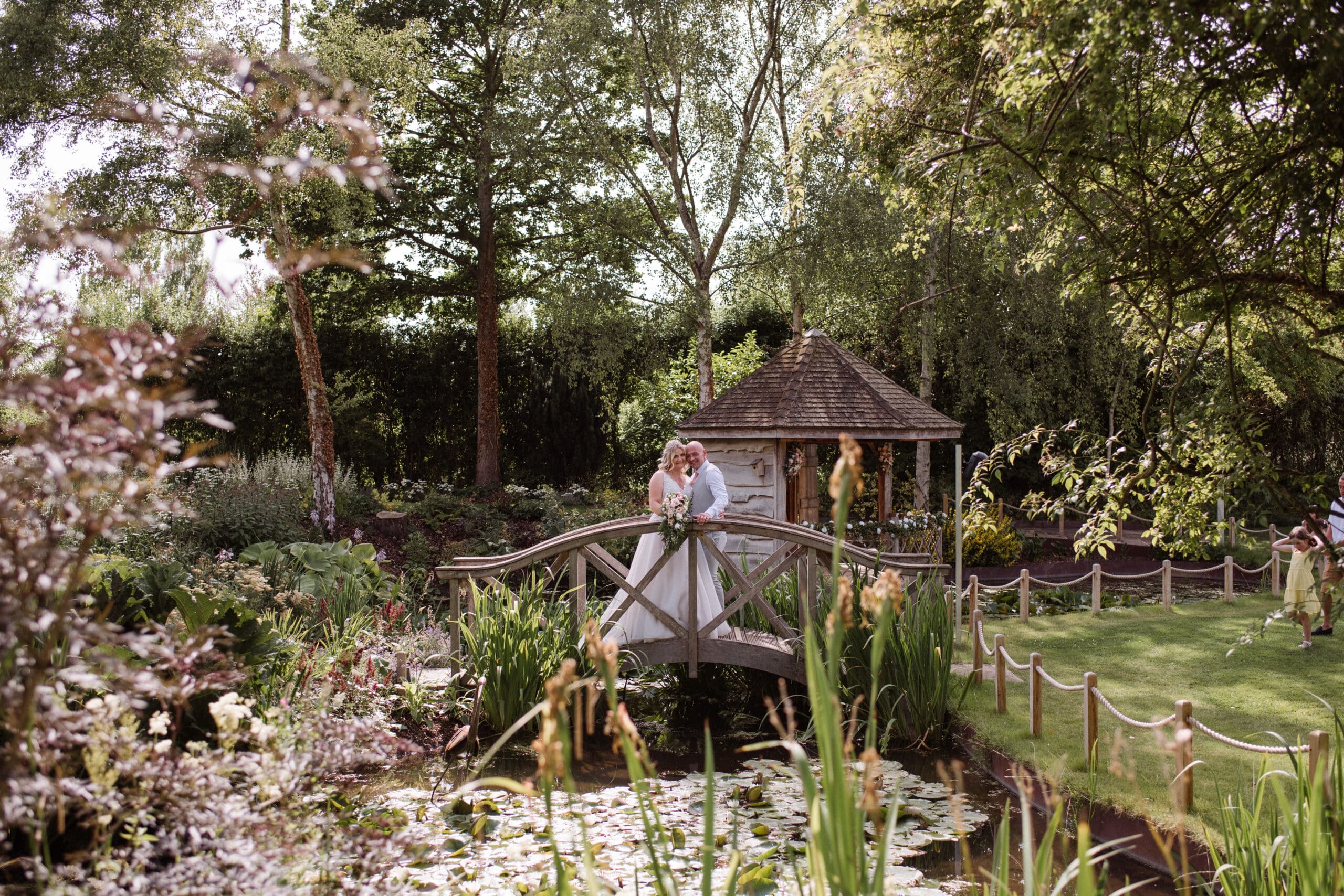 Just married couple on garden bridge over small pond in summer countryside wedding venue Gardens