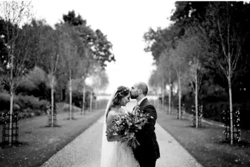 Just married couple share a special moment at countryside wedding venue's tree lined driveway