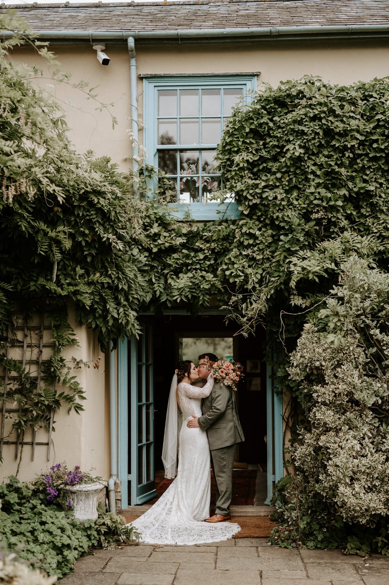 Country house wedding venue bride and groom kiss in blue doorway surrounded by green foliage at autumn wedding 