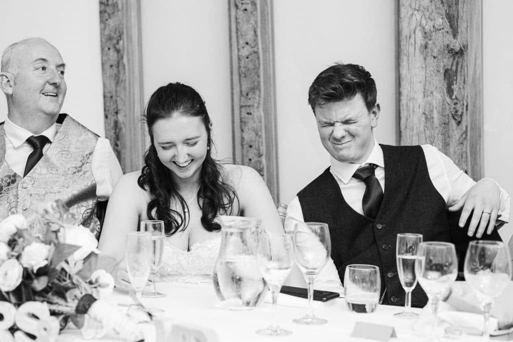 Bride and Groom on wedding day laughing together during wedding speeches at Barn Wedding Venue