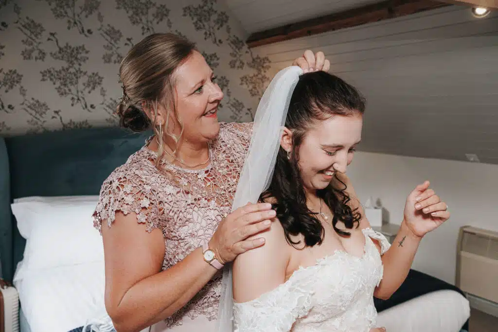 Bride and mother of the bride getting ready for wedding day and adjusting brides veil