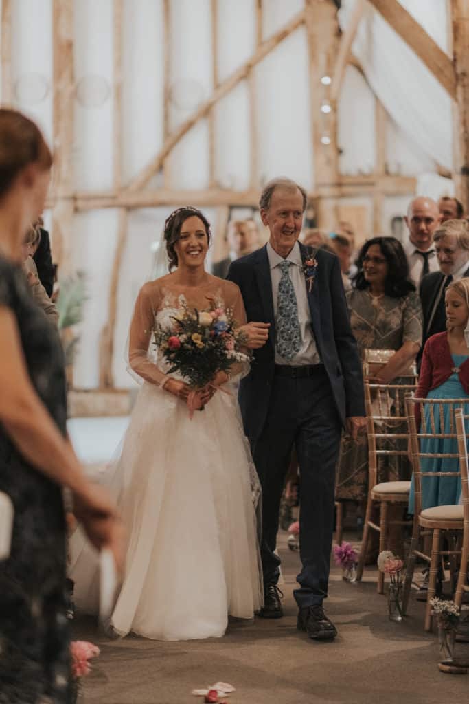 Bride enters wedding ceremony in rustic barn with father of the bride