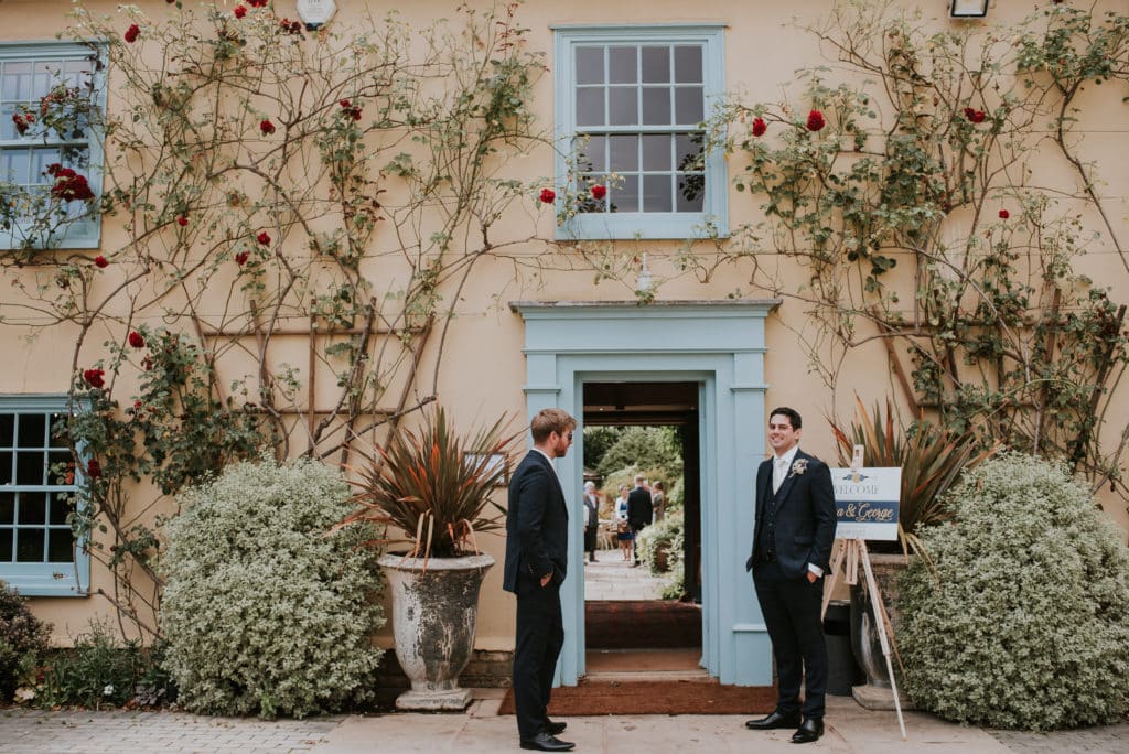 Ushers greet guests at country house wedding venue red roses growing around the blue front door 