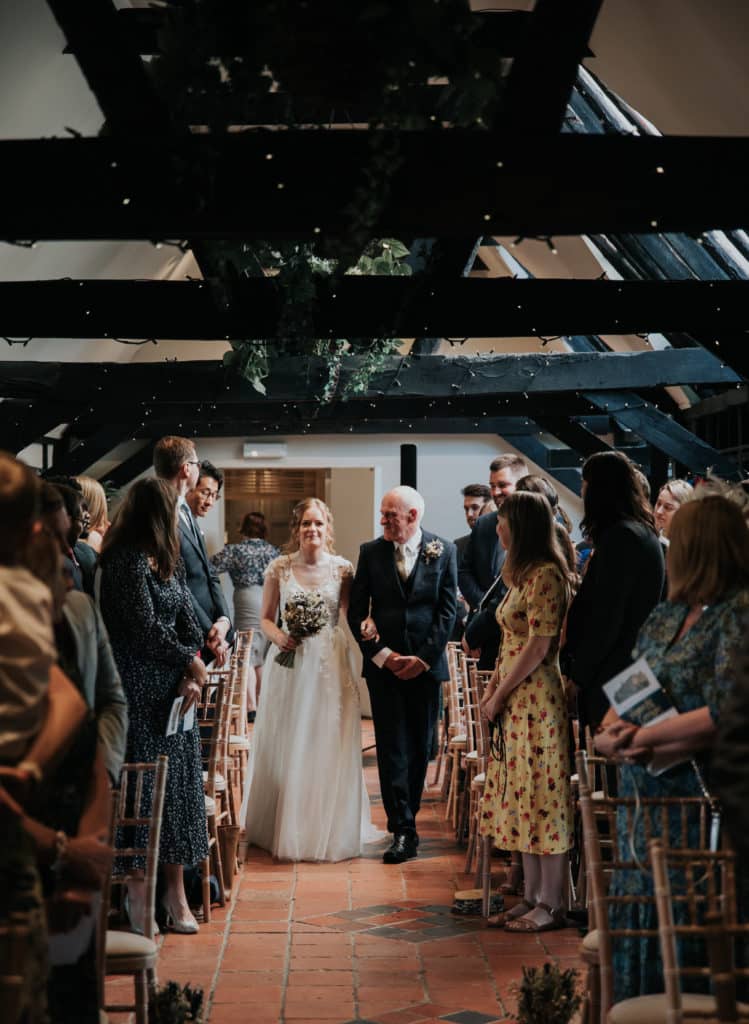 Bride enters ceremony with father of the bride and rustic barn wedding venue 