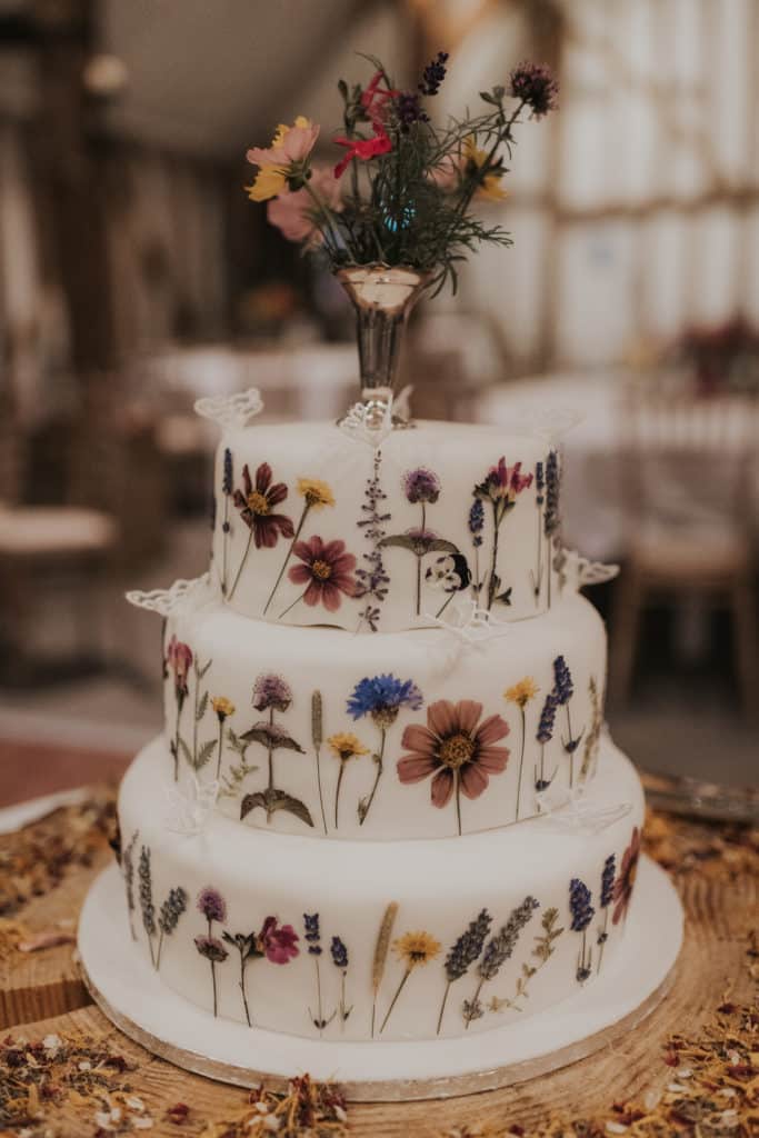 Three tier white wedding cake decorated with wildflowers at barn wedding venue