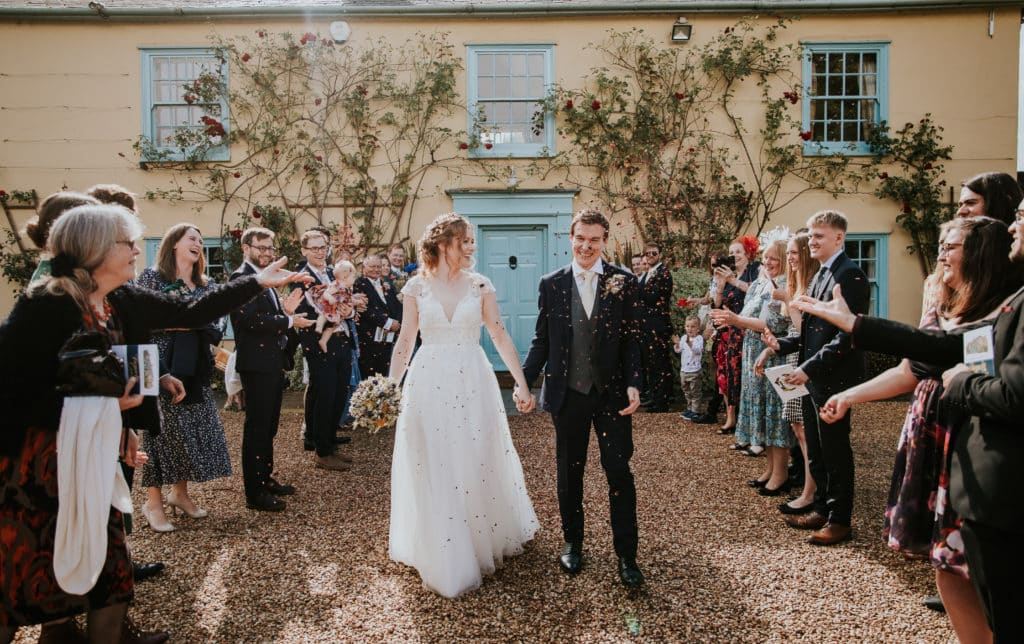 Bride and groom enjoy a confetti shower in front of country house wedding venue 