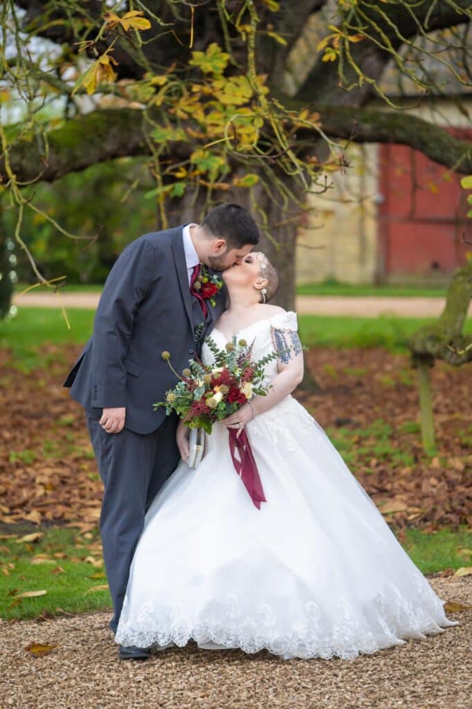 Beautiful bride and handsome groom kiss on wedding day at countryside wedding venue 