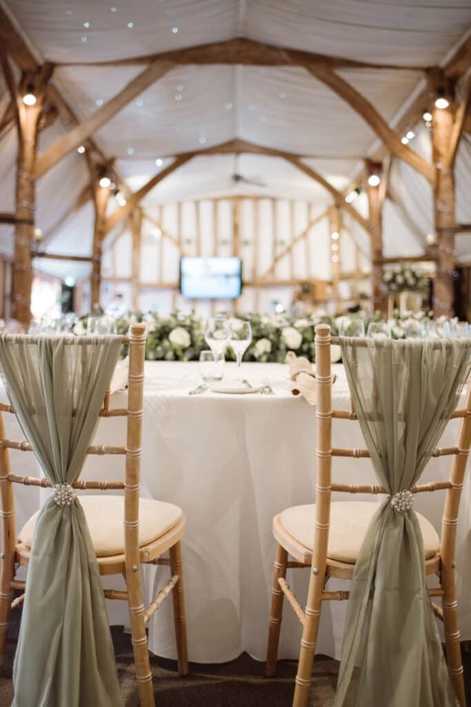 Rustic barn with pretty cream chairs and safe sashes set for wedding meal