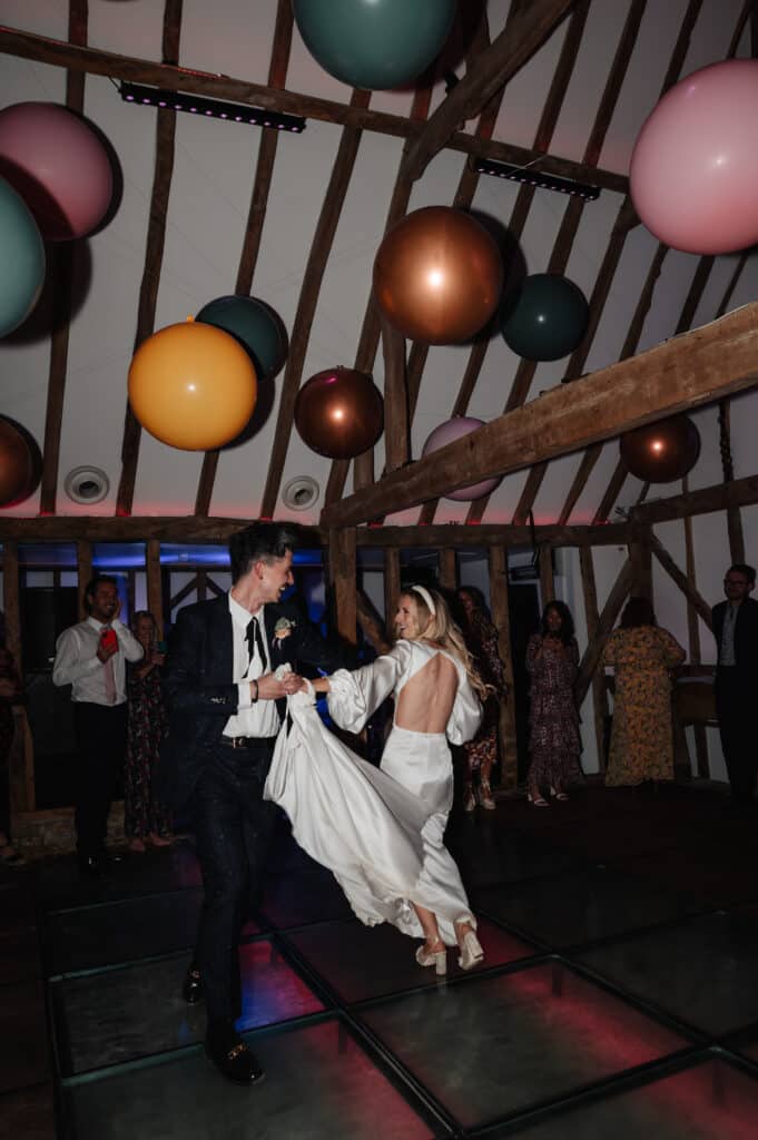 Bride and Groom first dance on wedding day in rustic barn with colourful overhead orb lanterns in gold, pink yellow and blue