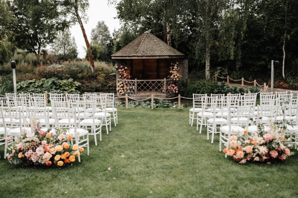 Garden wedding venue set for ceremony with white ceremony chairs and peach flower decorations set on garden lawns