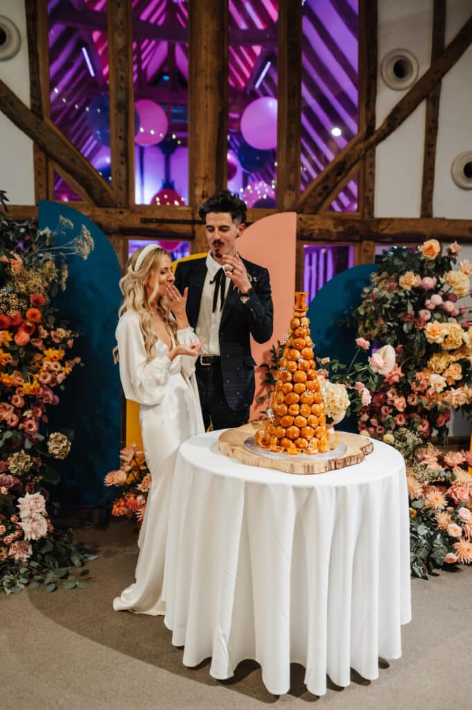 Bride and groom cut croquembouche wedding cake at rustic barn wedding venue