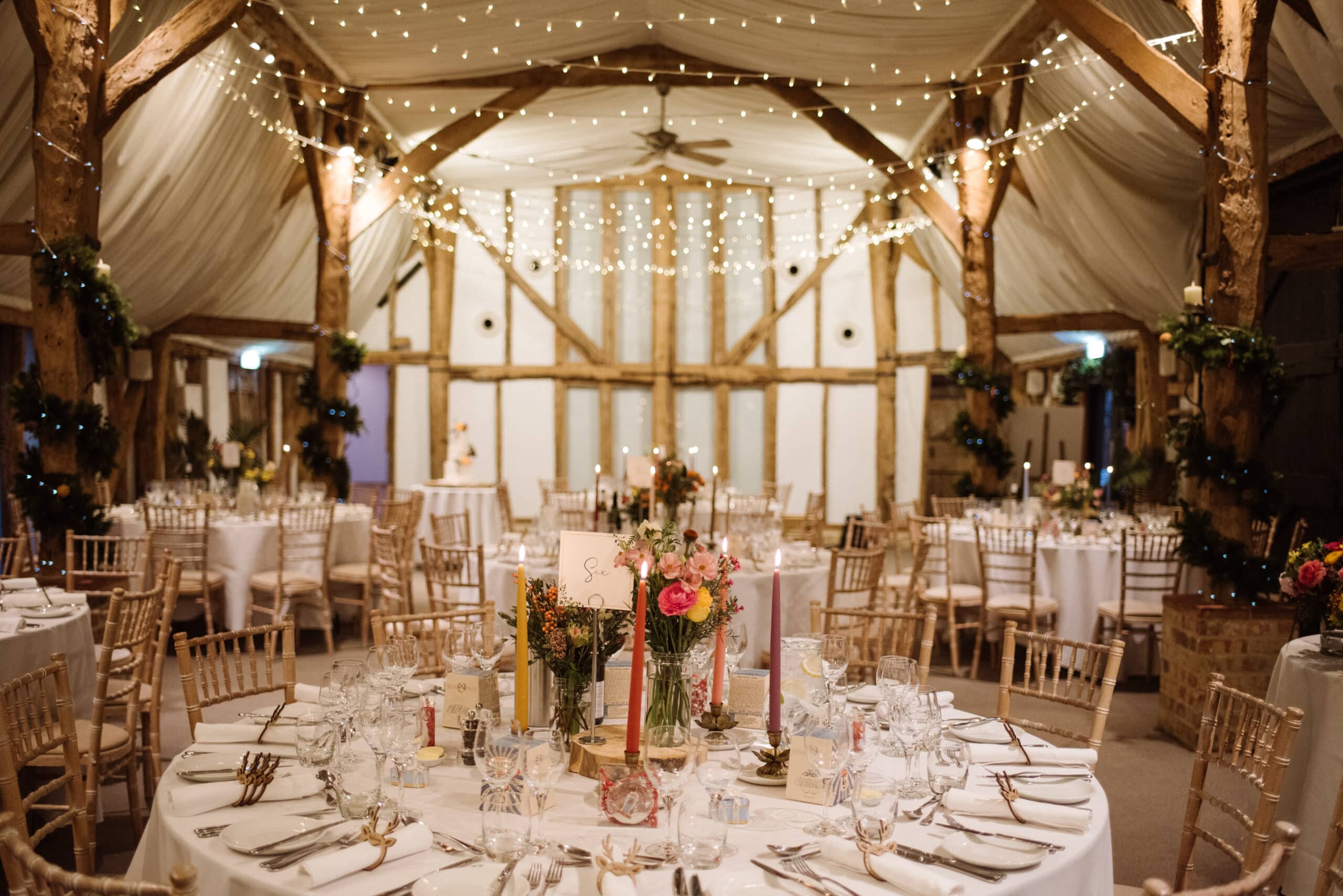Barn wedding venue set for meal with twinkly fairylights and floral decorations