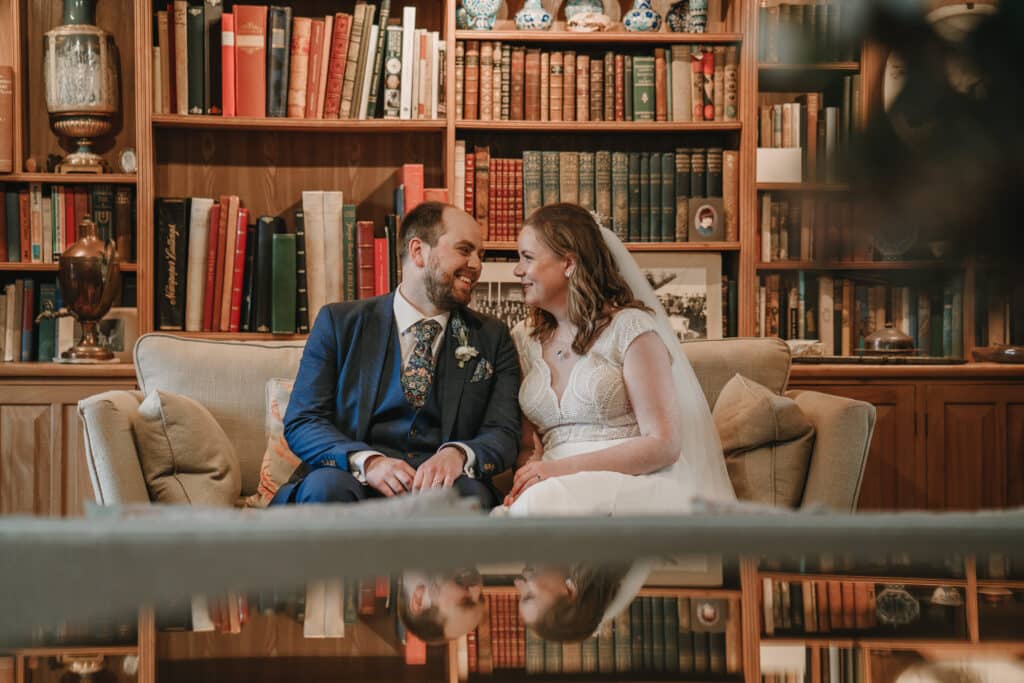 Bride and groom on wedding day in drawing room of country house in front of library bookshelves 