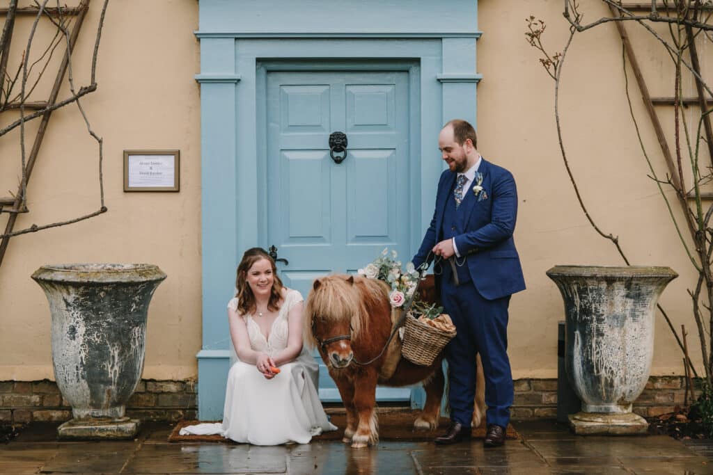 Bride and groom in front of blue door of country house wedding venue pose for photos with confetti pony