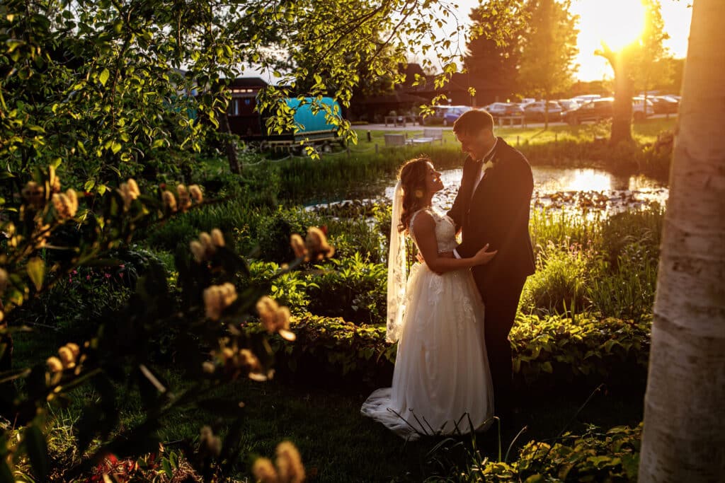 Couple enjoy a golden hour sunset on their wedding day by lake with flowers in the foreground
