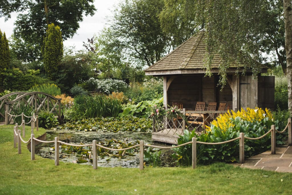 Pretty garden summerhouse set across pond with lilies pads and flowers at countryside wedding venue 