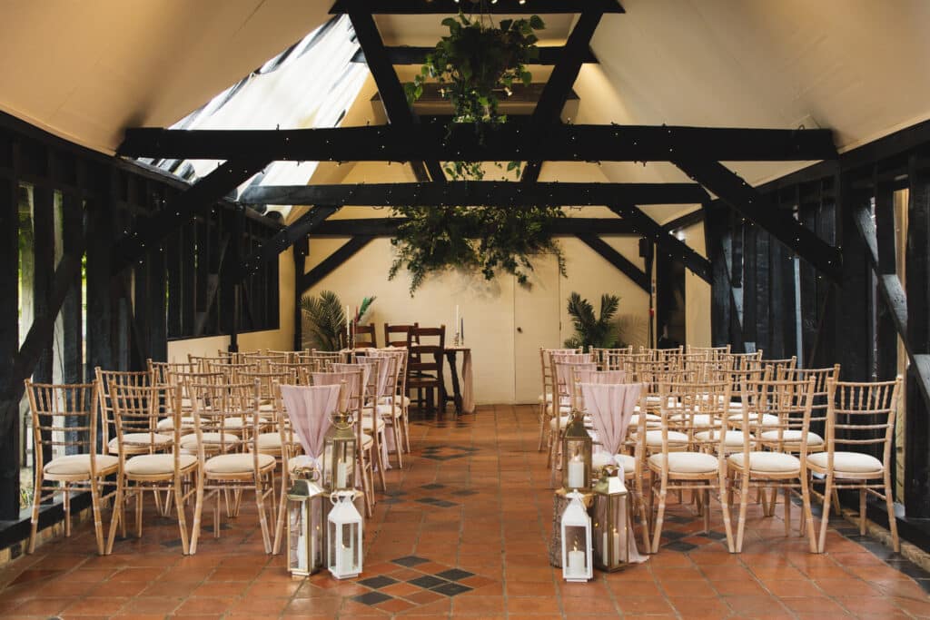 Rustic Wedding barn set for ceremony with black timber beans and pretty storm lanterns, cancels and chair sashes