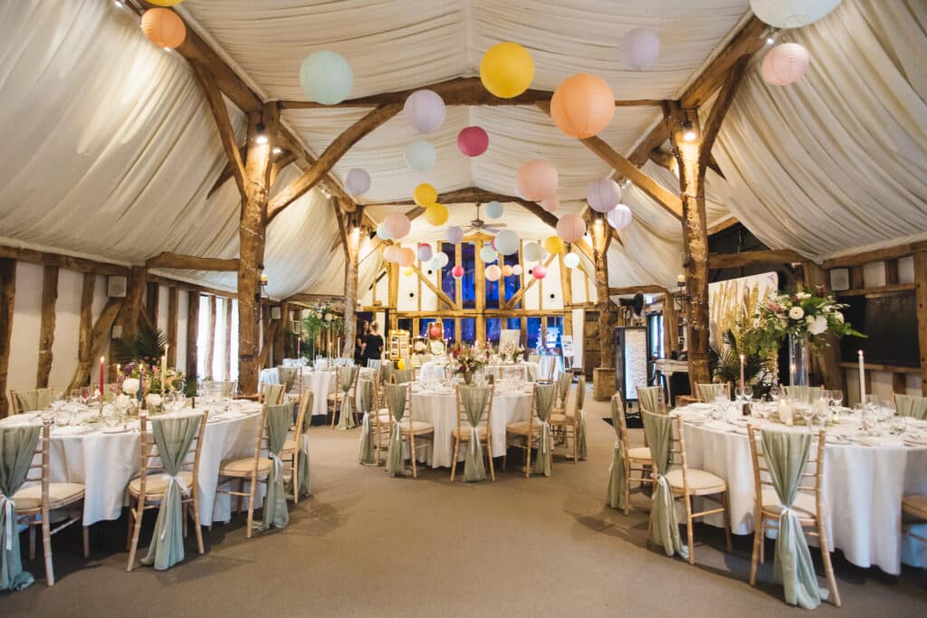 Rustic Barn Wedding venue with colourful paper ceiling lanterns and pretty decorations and pastel flowers set for wedding meal