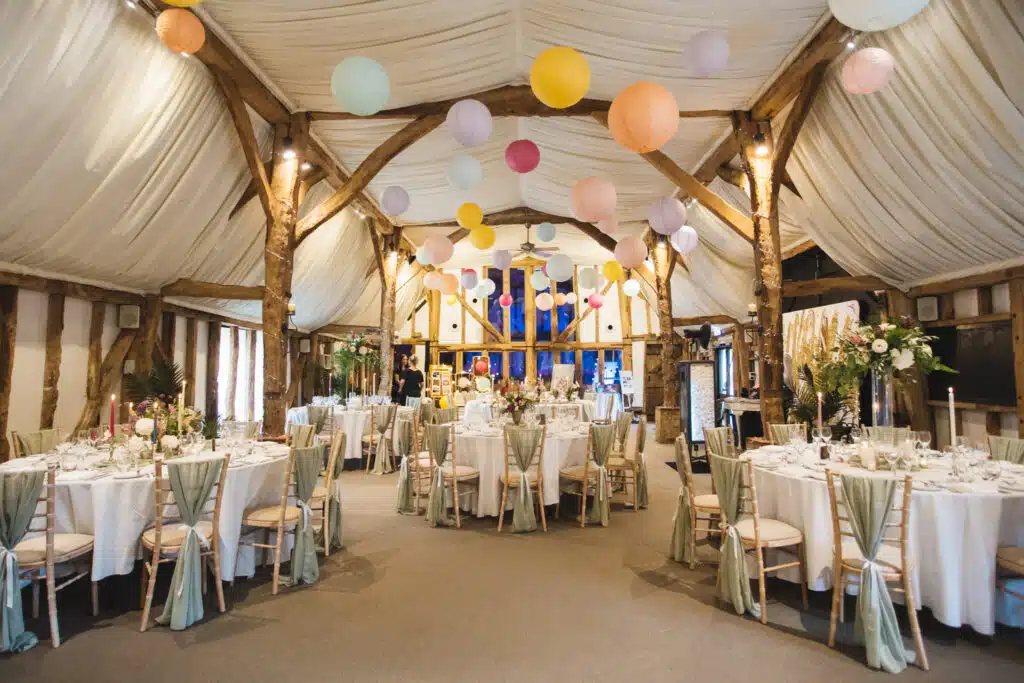 Rustic Barn Wedding venue with colourful paper ceiling lanterns and pretty decorations and pastel flowers set for wedding meal 