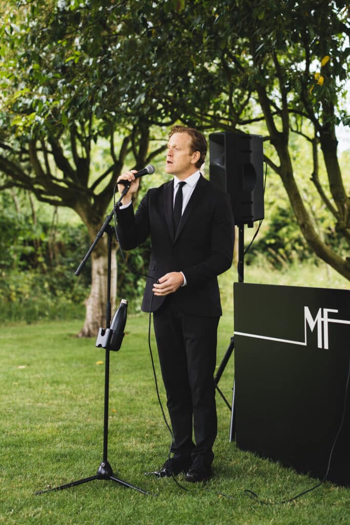 Male swing singer performing in black suit and tie in garden of wedding venue 